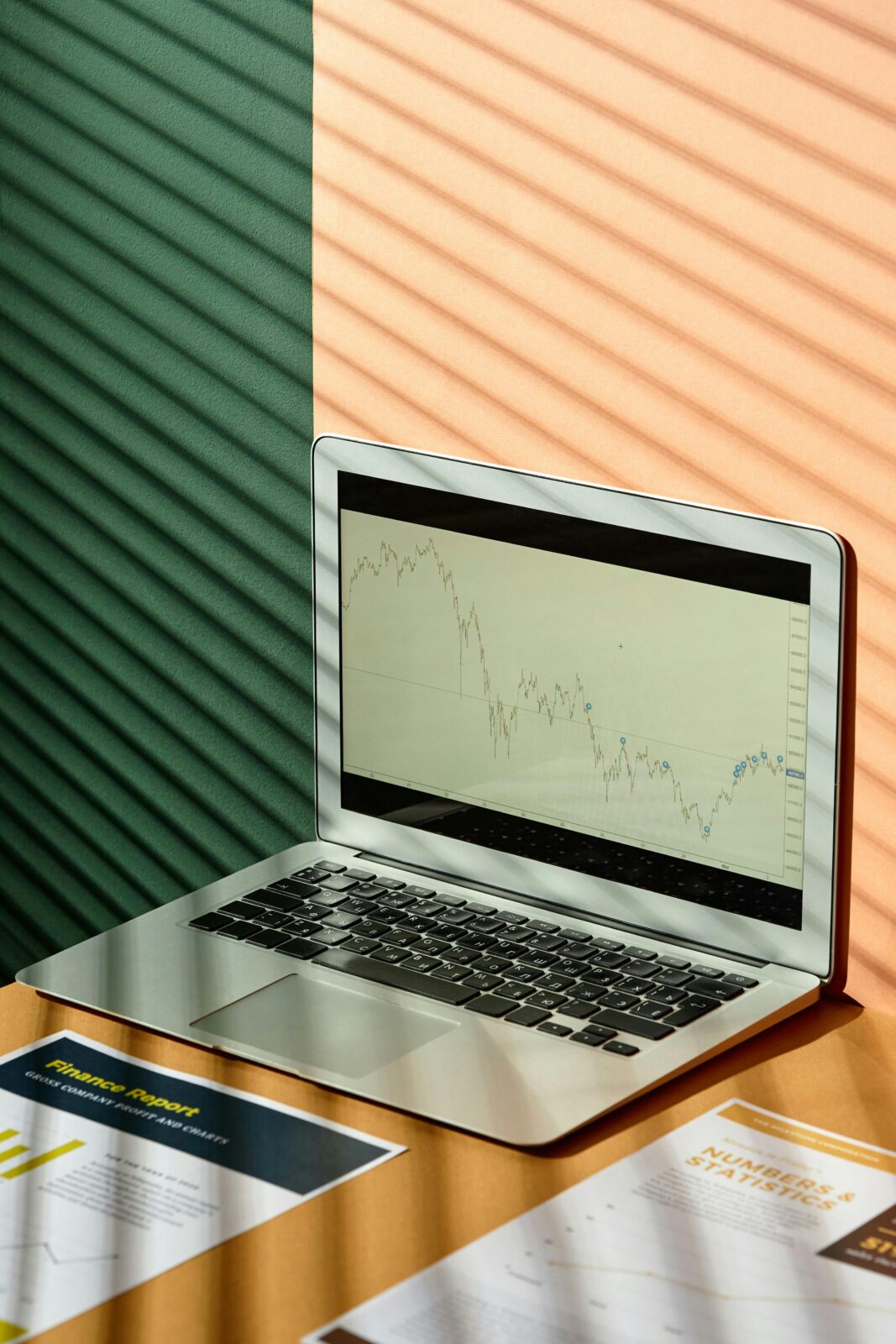 A laptop displaying financial graphs with documents on a sunlit office desk, ideal for finance themes.